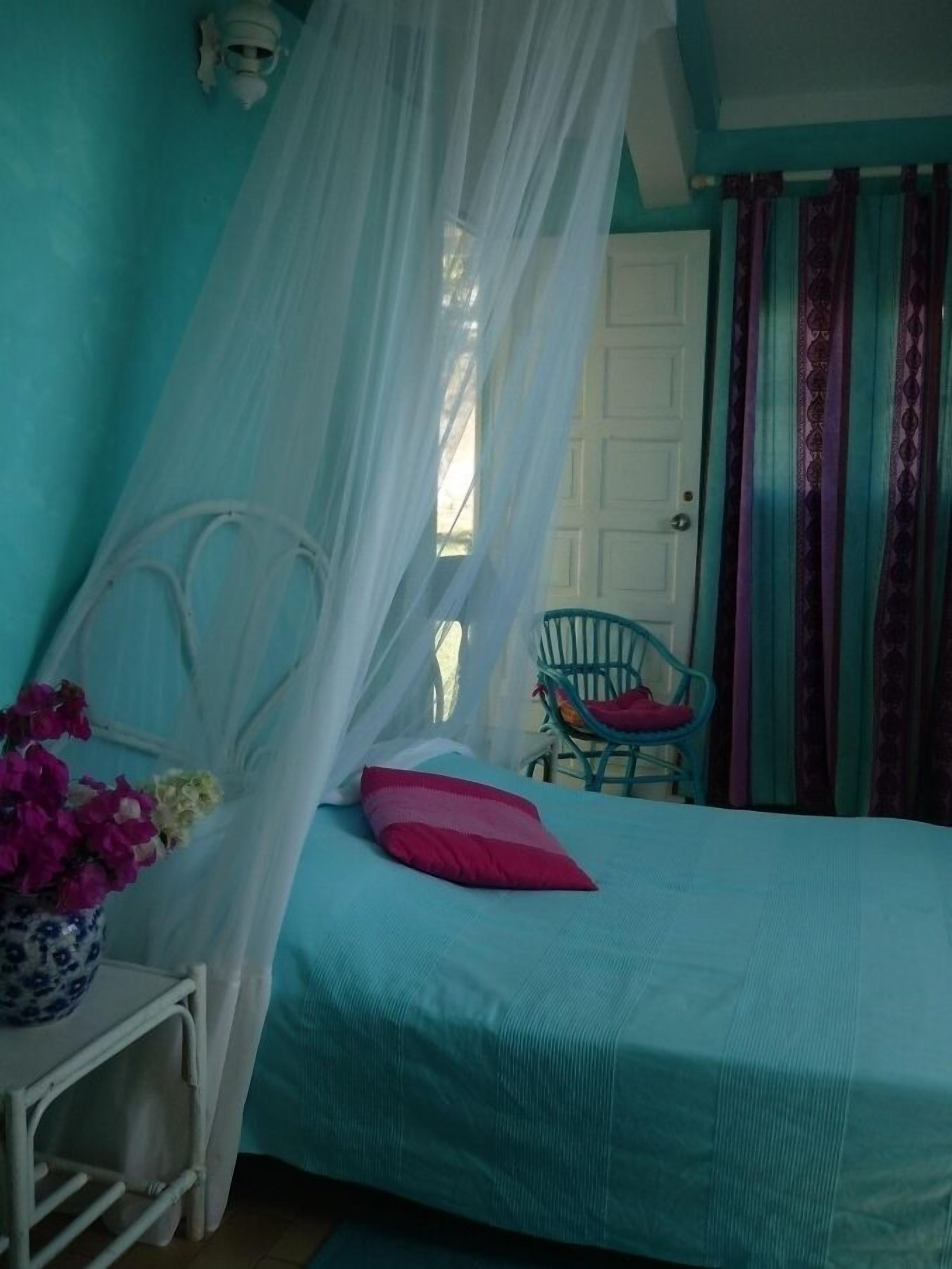 A bedroom with a bed, a chair, a bedside table, and a window with curtains.