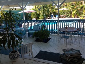 A covered patio area with a pool, outdoor seating, and potted plants. - Cap Sud Caraïbes Hôtel (Le Gosier)