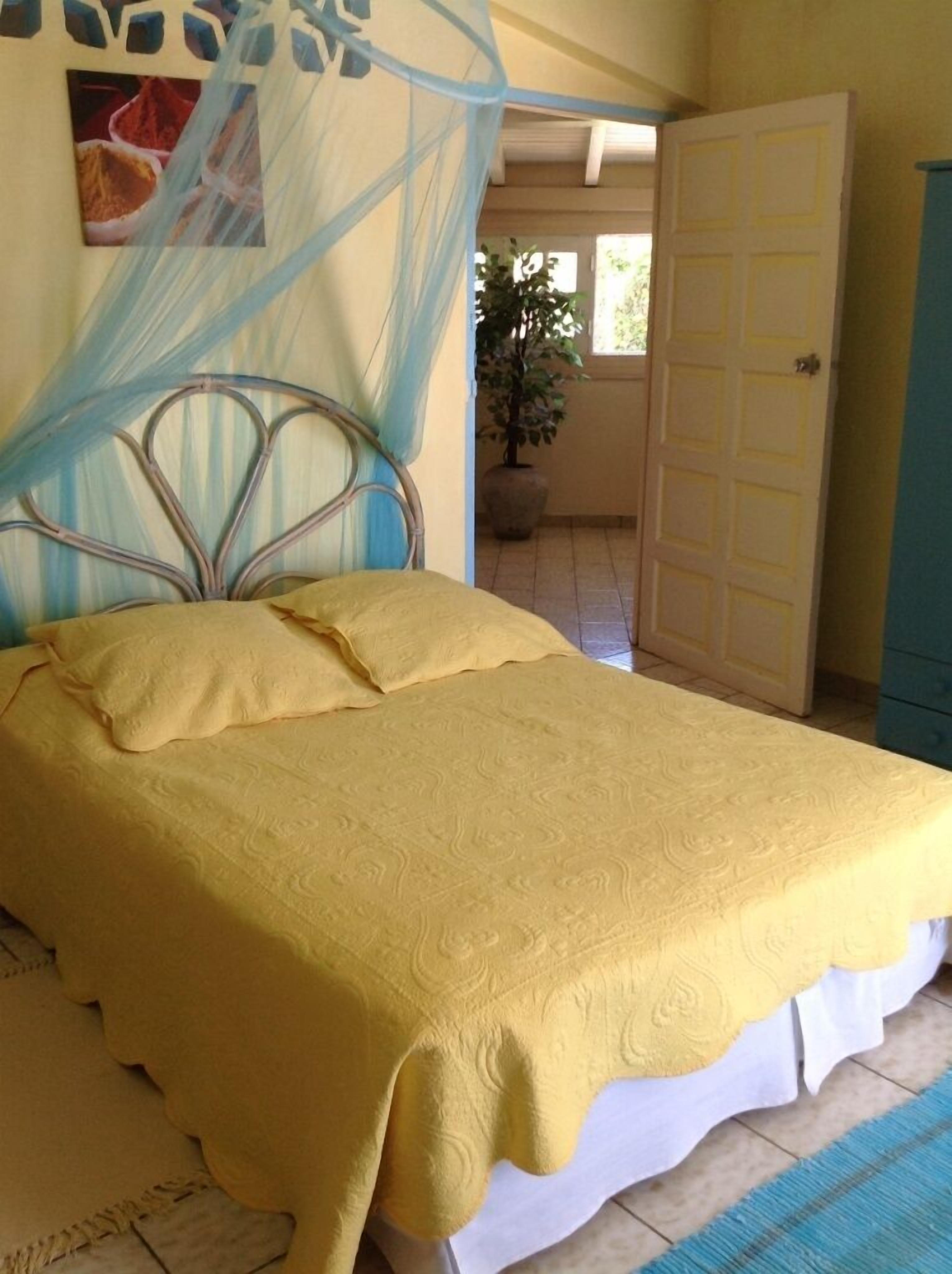 Una cama con colcha amarilla, cabecero de metal y dosel azul.