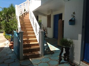 Una escalera que conduce a un edificio con una puerta azul, plantas en macetas y un suelo de baldosas de piedra.