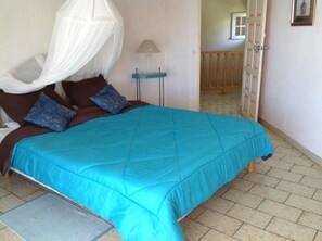 Un dormitorio con cama, mesita de noche, lámpara y puerta que da a otra habitación.