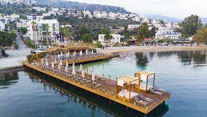 A waterfront pier with lounge chairs and umbrellas, a wooden deck, and a view of a hillside town in the background. - Hotel Vita Bella Resort & Spa (Bodrum)