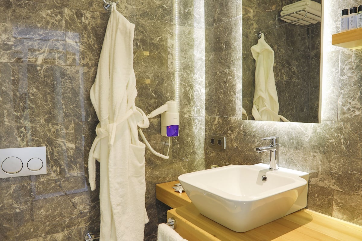 Een moderne badkamer met een marmeren wand, een wit wastafelmeubel, een toilet en een badjas die aan een rek hangt.