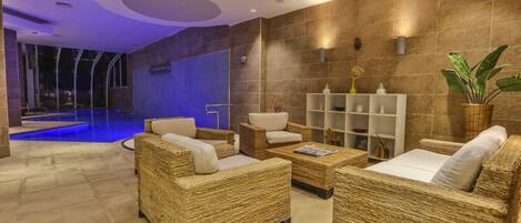 Un área de descanso moderna con mobiliario de mimbre, piscina e interior bien iluminado.