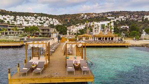 A wooden pier with lounge chairs and umbrellas, leading to a beach area with thatched umbrellas and a view of a coastal town. - Hotel Vita Bella Resort & Spa (Bodrum)