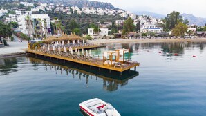 A floating bar with lounge chairs and umbrellas, a docked boat, and a calm waterfront with buildings in the background. - Hotel Vita Bella Resort & Spa (Bodrum)