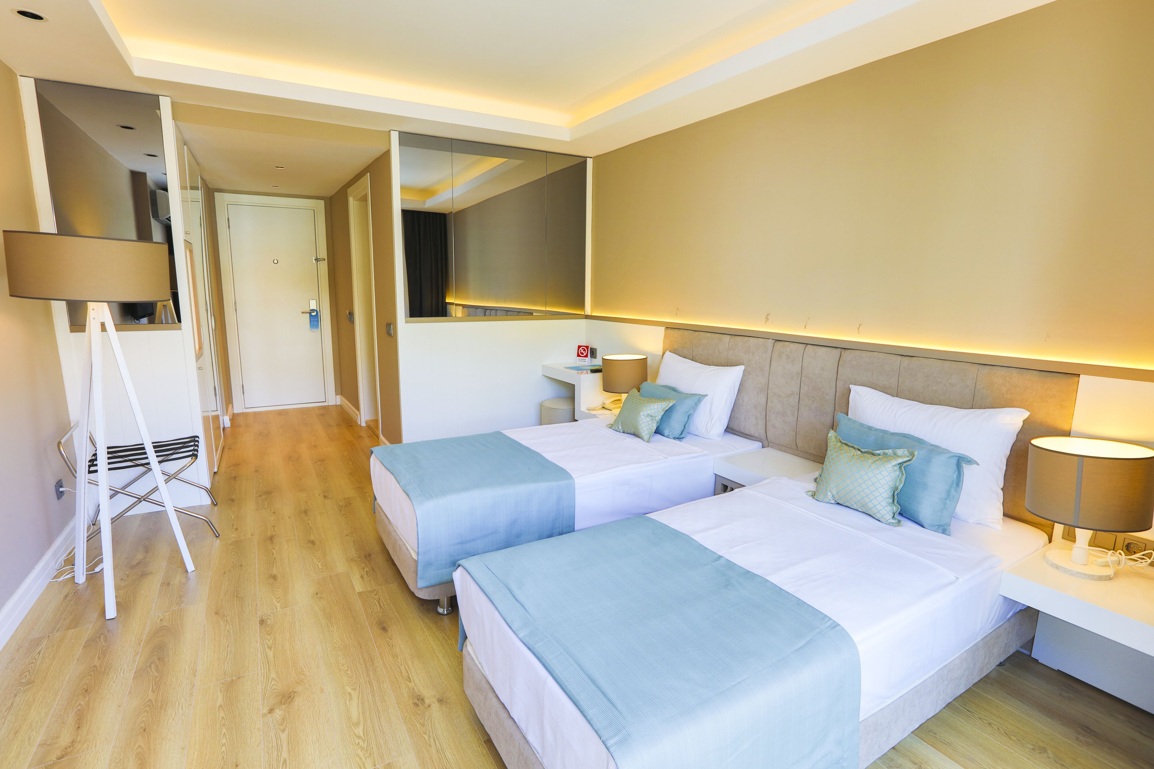 A hotel room with two beds, a bedside table with a lamp, a mirror, and a whiteboard.