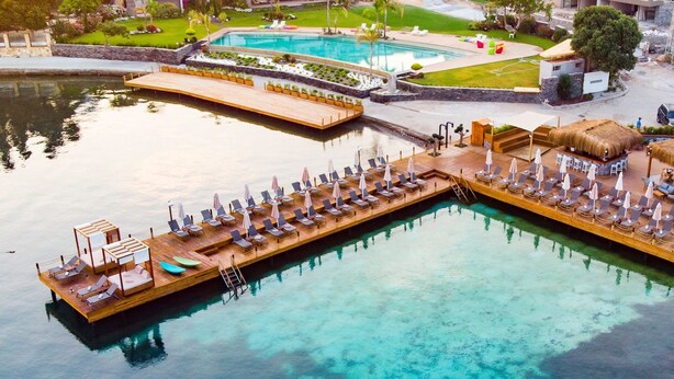 An aerial view of a resort with a wooden dock leading to a pool area, a separate lounge area with thatched umbrellas, and a small bar. - Hotel Vita Bella Resort & Spa (Bodrum)