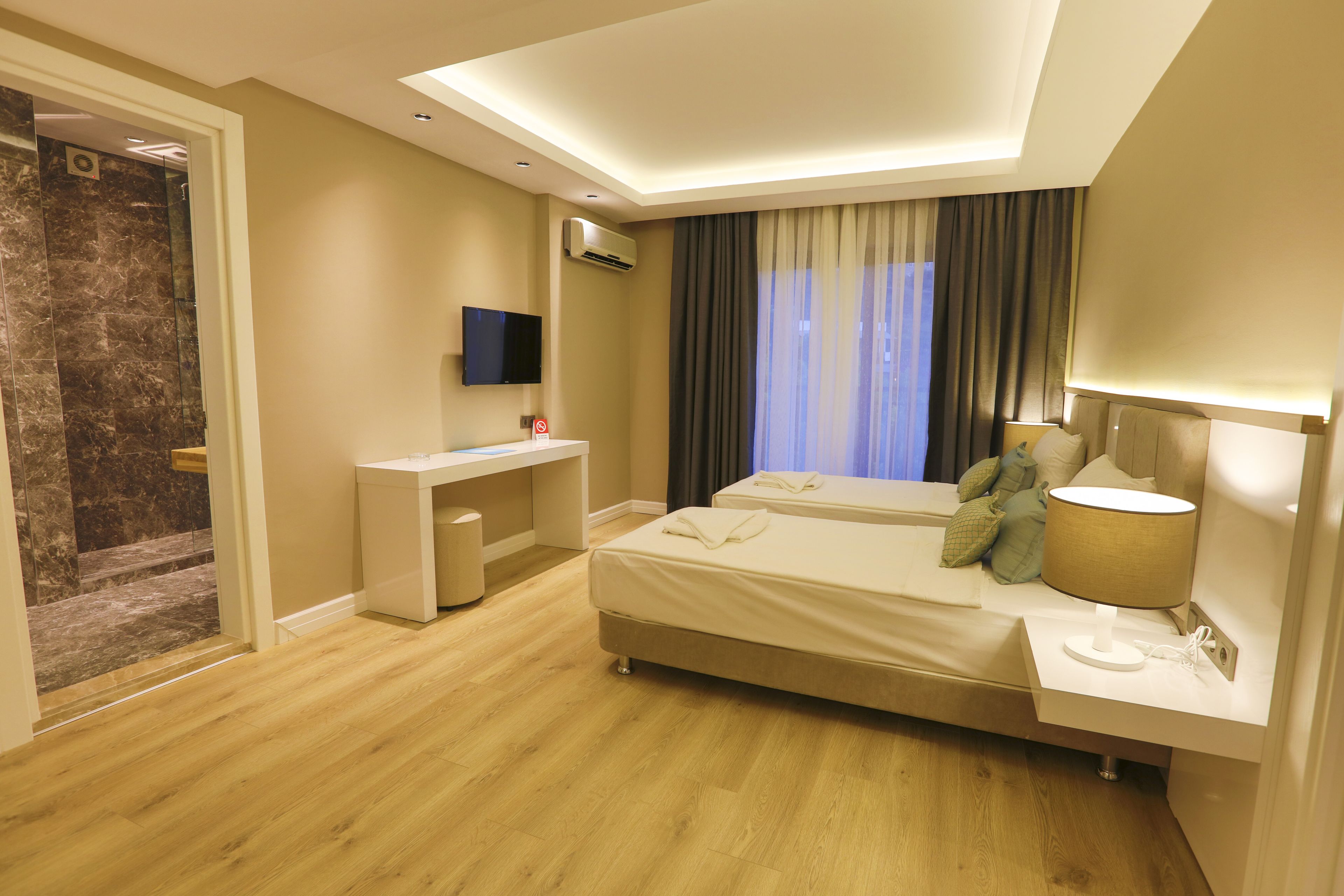 A modern hotel room with a bed, bedside table, and a desk with a chair.