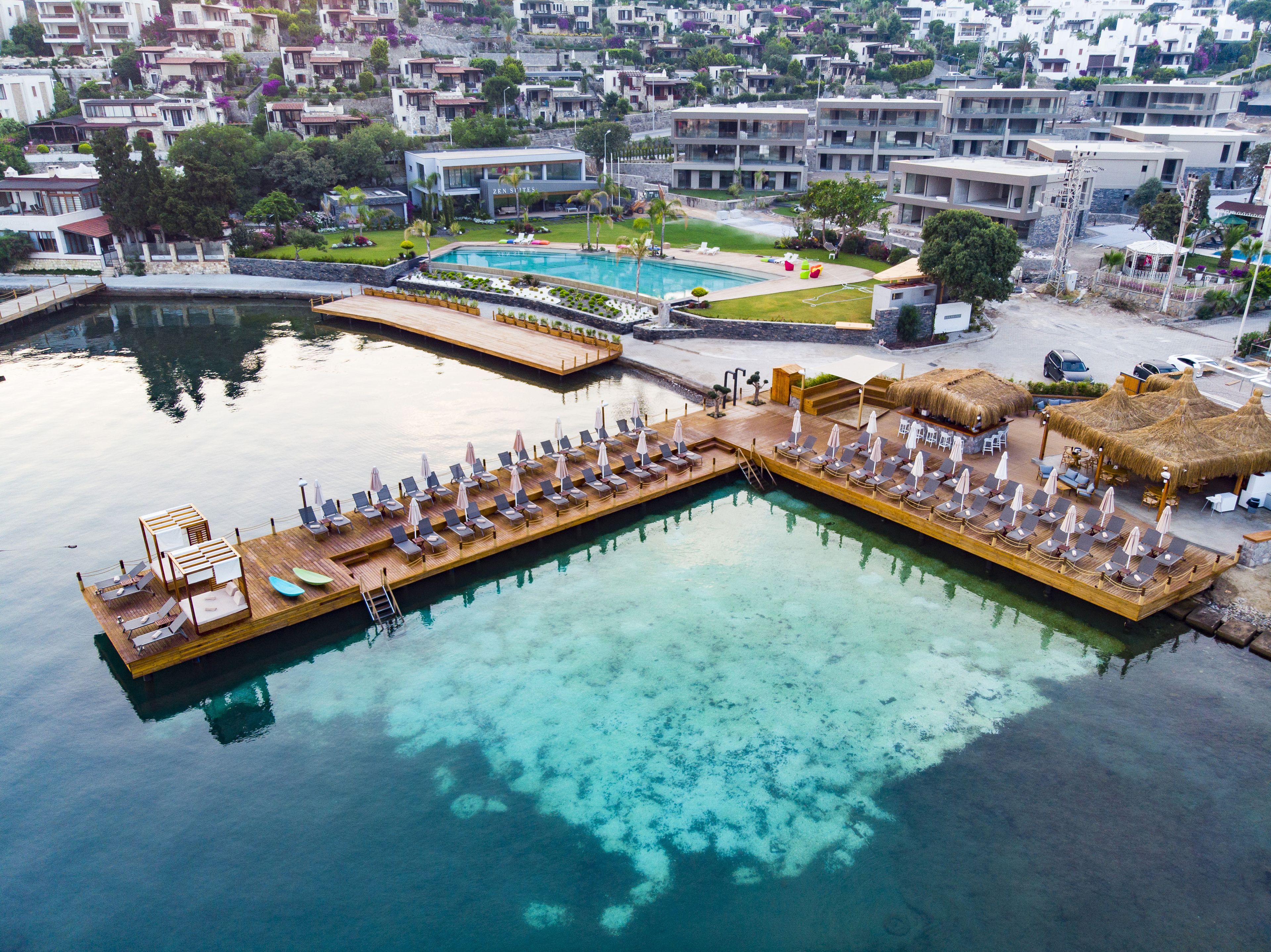 A waterfront hotel with a pool, lounge area, and thatched-roof outdoor seating.