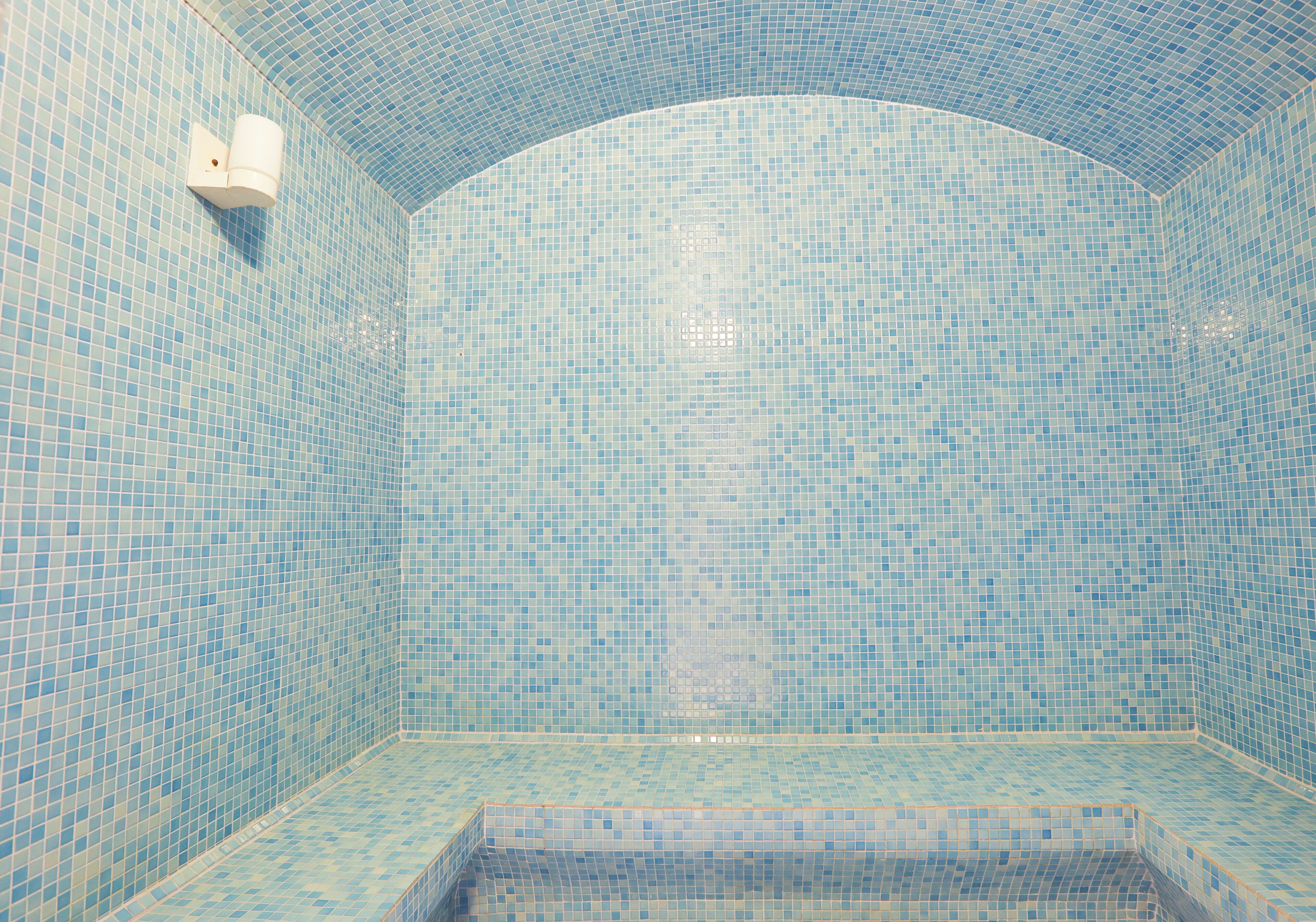 Un baño con mosaicos azules, un dispensador de toallas blanco y una bañera.