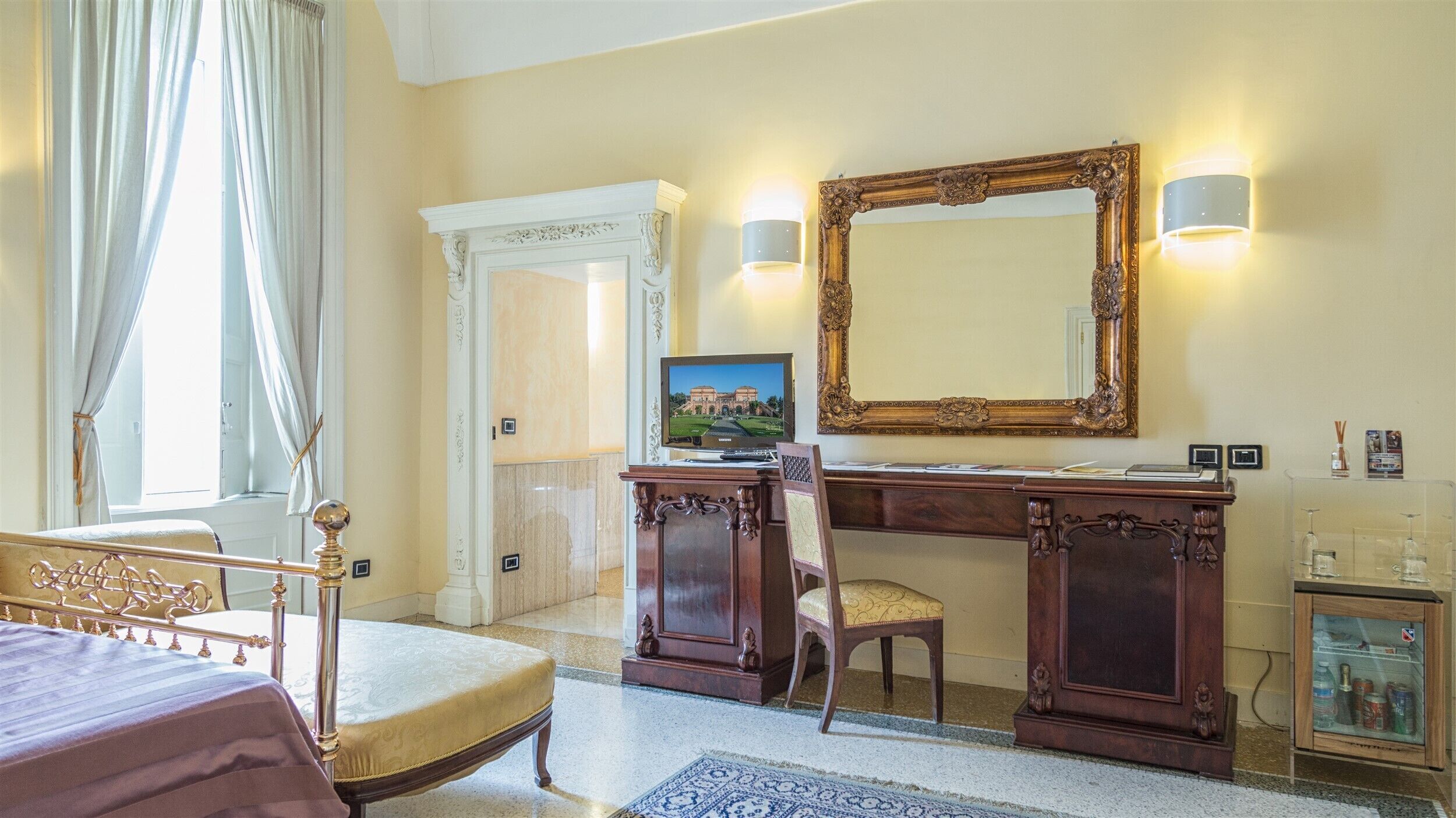 Una habitación de hotel con cama, escritorio con ordenador, silla, espejo grande y pequeño armario.