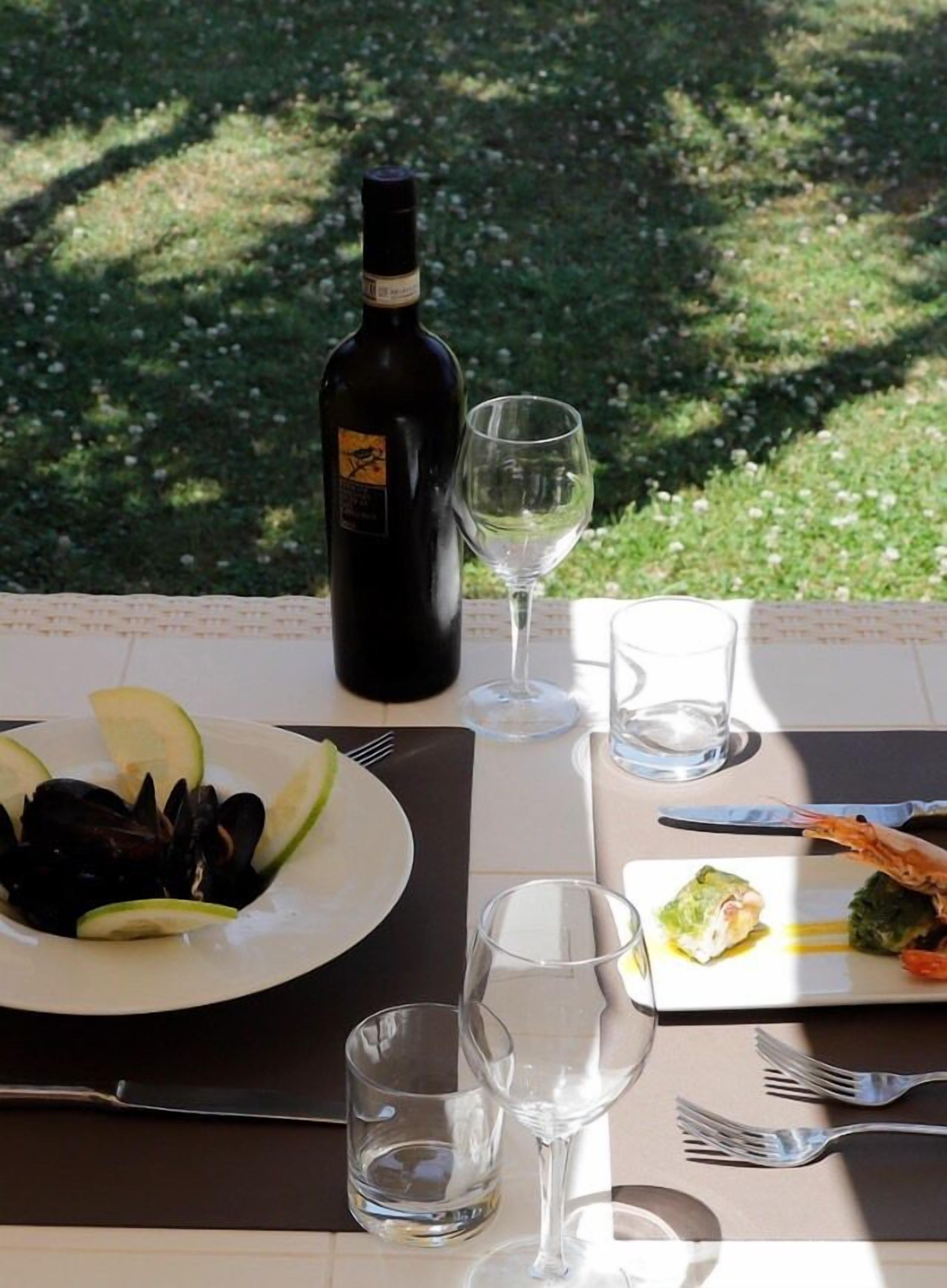 Ein Tisch im Freien mit einer Weinflasche, Gläsern und Tellern voller Essen.