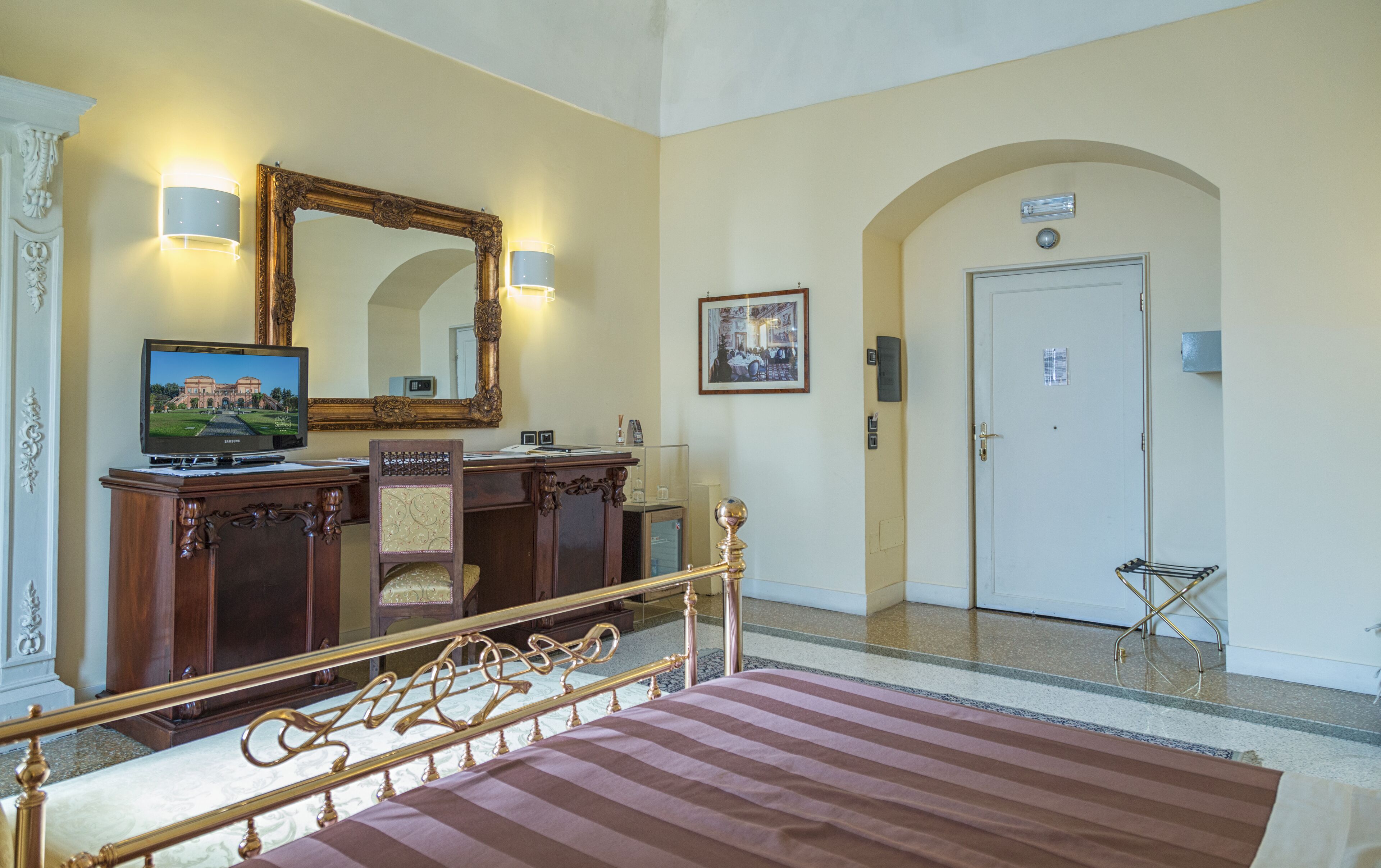 Una habitación de hotel con una cama, un escritorio con ordenador, un espejo grande y una puerta.