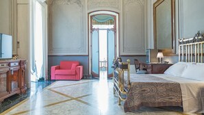 A spacious room with a large bed, a red armchair, and a wooden dresser. - Villa Signorini Events & Hotel (Ercolano)