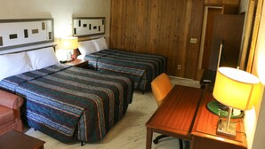 Ein Hotelzimmer mit zwei Betten, einem Holztisch, einem Stuhl, einer Lampe und einem Spiegel.