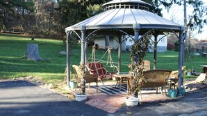 Ein Pavillon mit Schaukelstuhl und Tisch, umgeben von Kübelpflanzen und Gartenmöbeln.