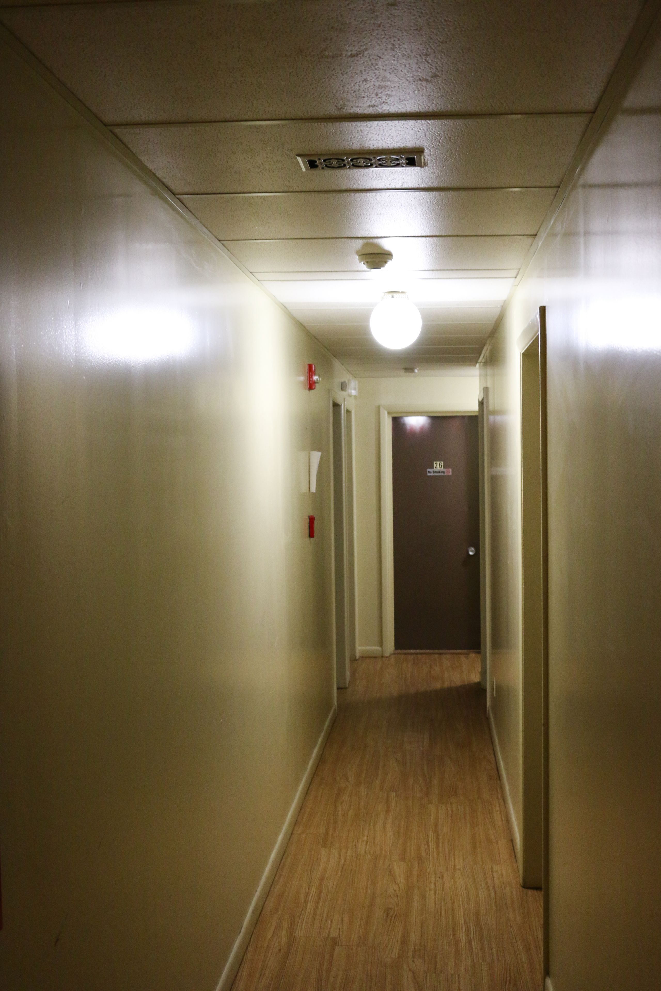 A narrow, well-lit hallway with wooden flooring and a door at the end.