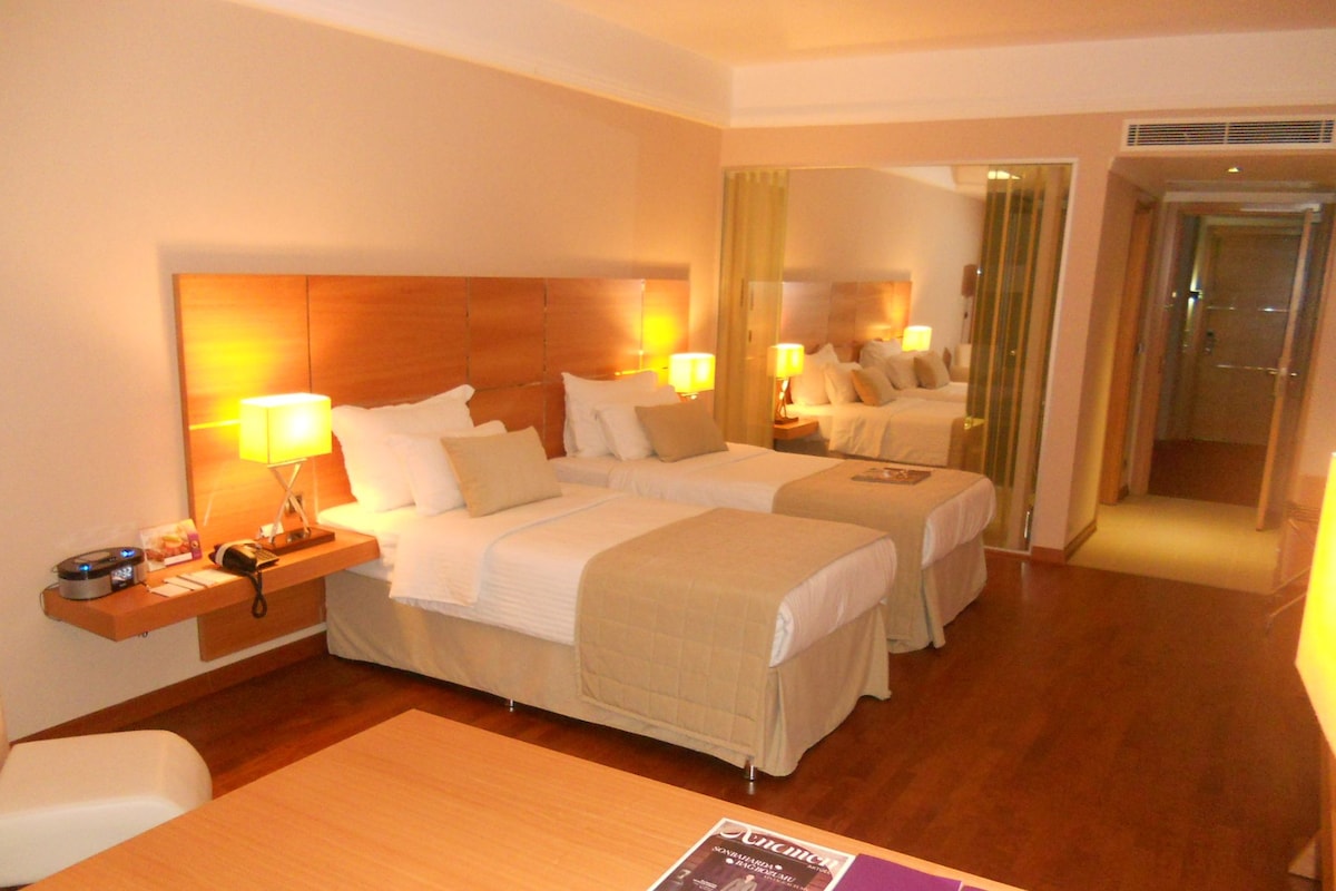 Una habitación de hotel con dos camas, mesitas de noche, lámparas, un espejo y suelo de madera.