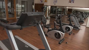A gym with multiple treadmills and exercise bikes, wooden flooring, and a large mirror wall.