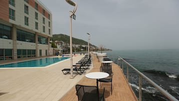 Eine Terrasse mit Sitzgelegenheiten im Freien, einem Pool und Blick auf das Meer.