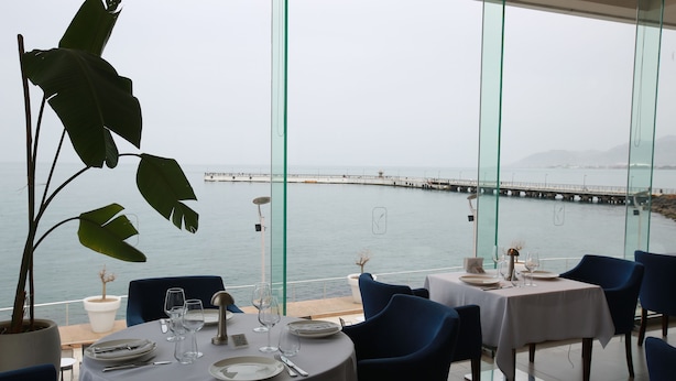 Restaurante com mesas redondas preparadas para refeições, com vista para um corpo de água e um cais.