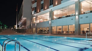 Um hotel moderno com piscina, vários andares e janelas amplas.