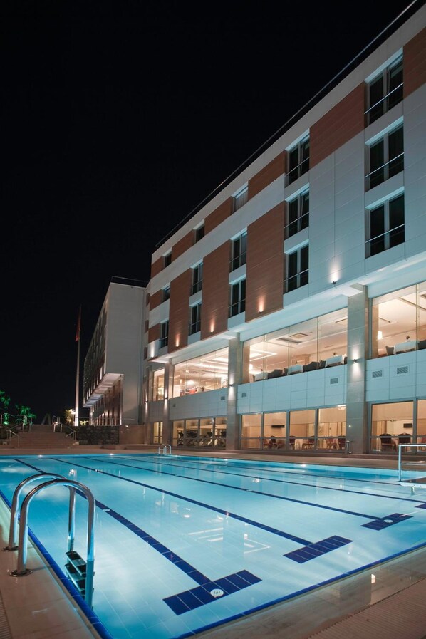 Un hotel moderno con piscina, varios pisos y amplias ventanas.