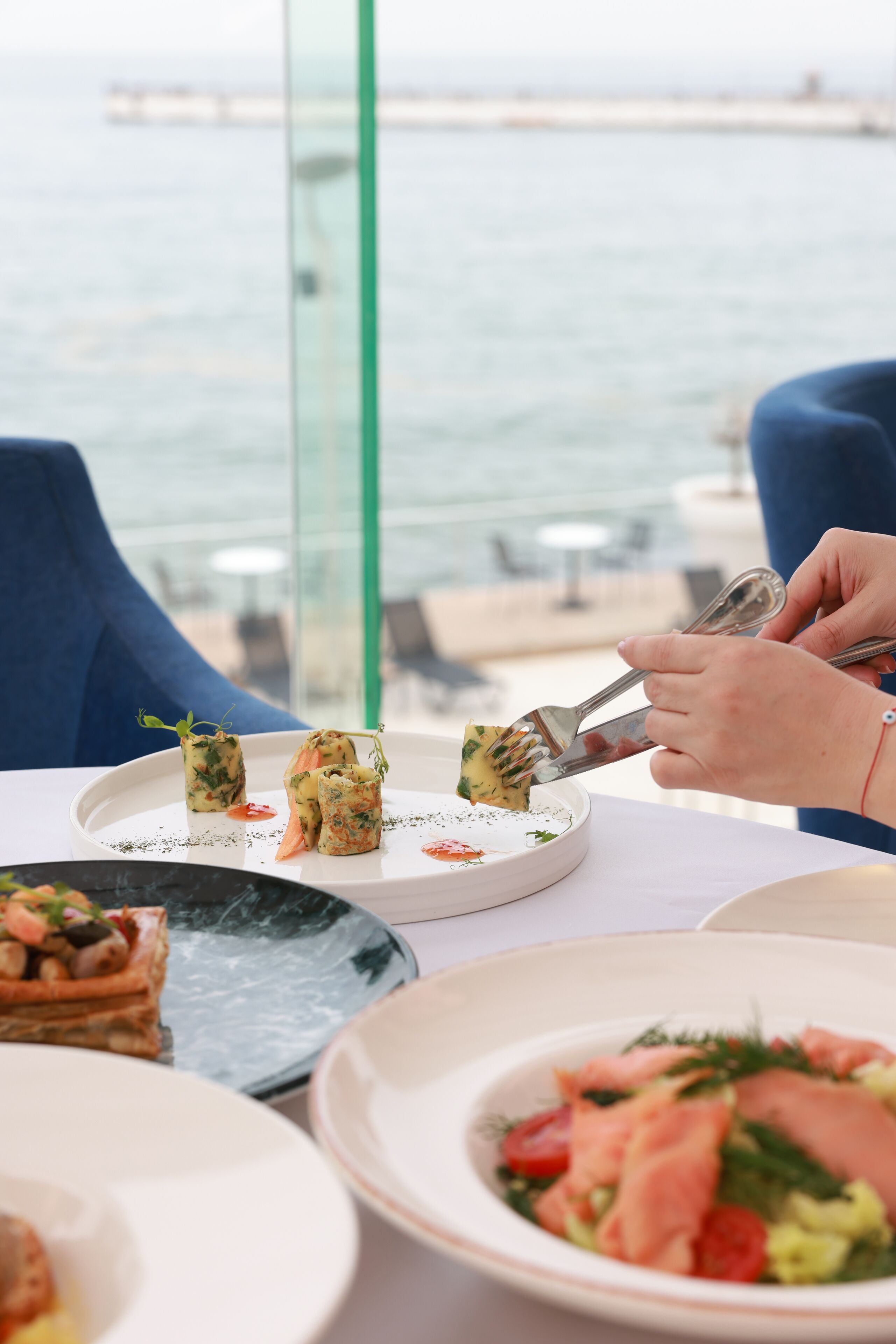 A dining table with various dishes, including a plate with rolled appetizers and a plate with salmon and vegetables.