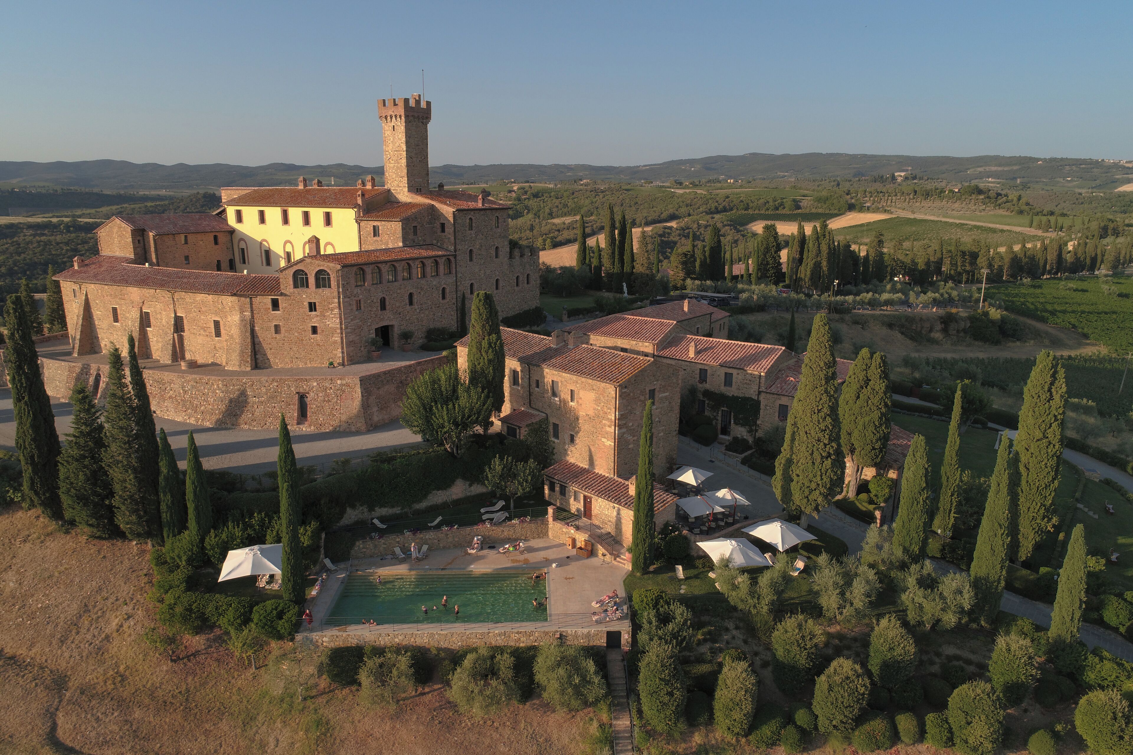 A large historic building with a tower, surrounded by trees and a swimming pool.