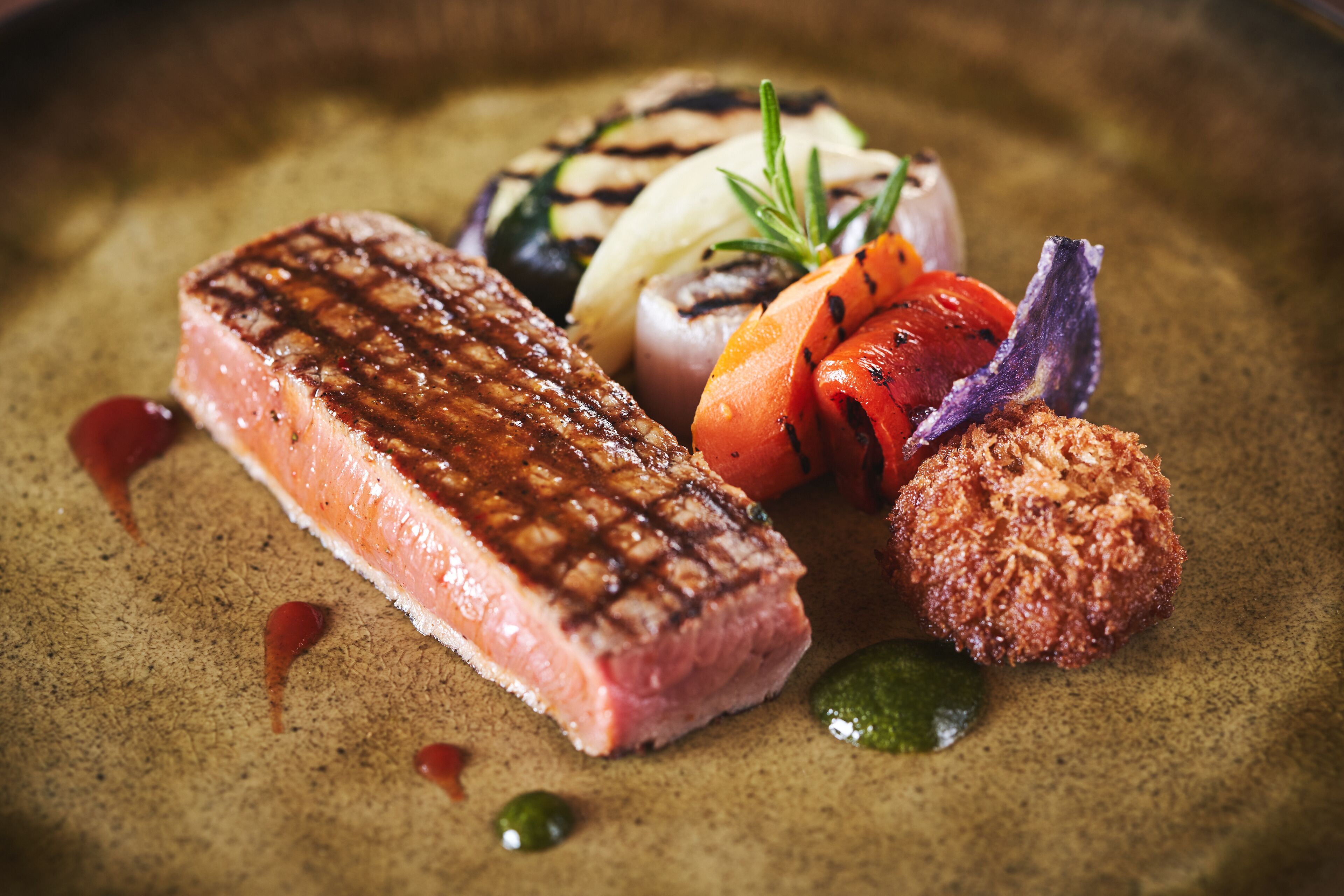 A steak with grill marks, grilled vegetables, and a small round item on a plate.