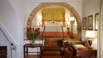 Una camera da letto con un arco in mattoni, un letto a baldacchino, lampade ai comodini, una scrivania con una sedia e un vaso con fiori.