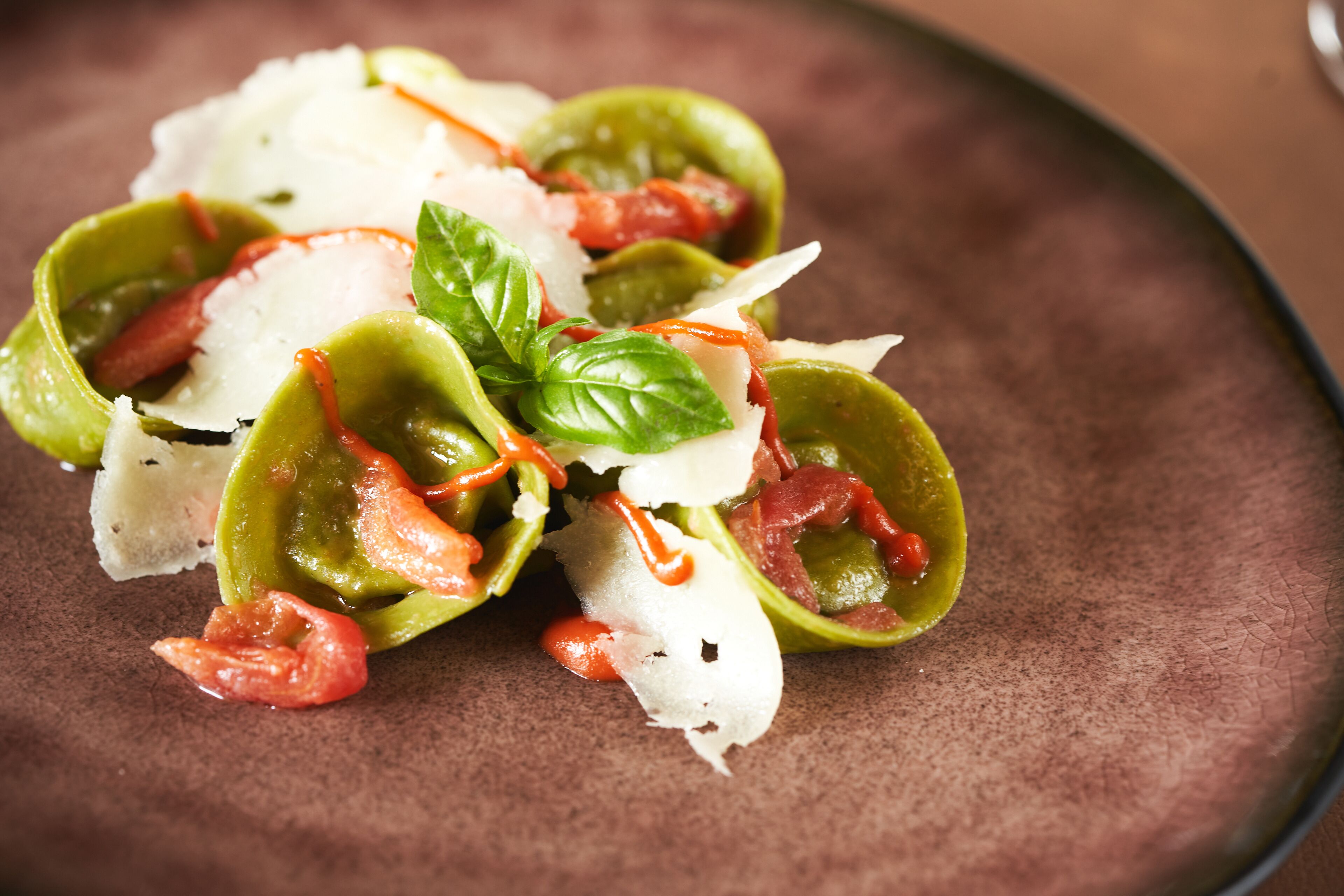 A dish with green vegetables, cheese, and basil on a brown plate.