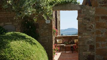 Un arco de piedra que da a un patio con una mesa y sillas, rodeado de macetas con plantas y flores.