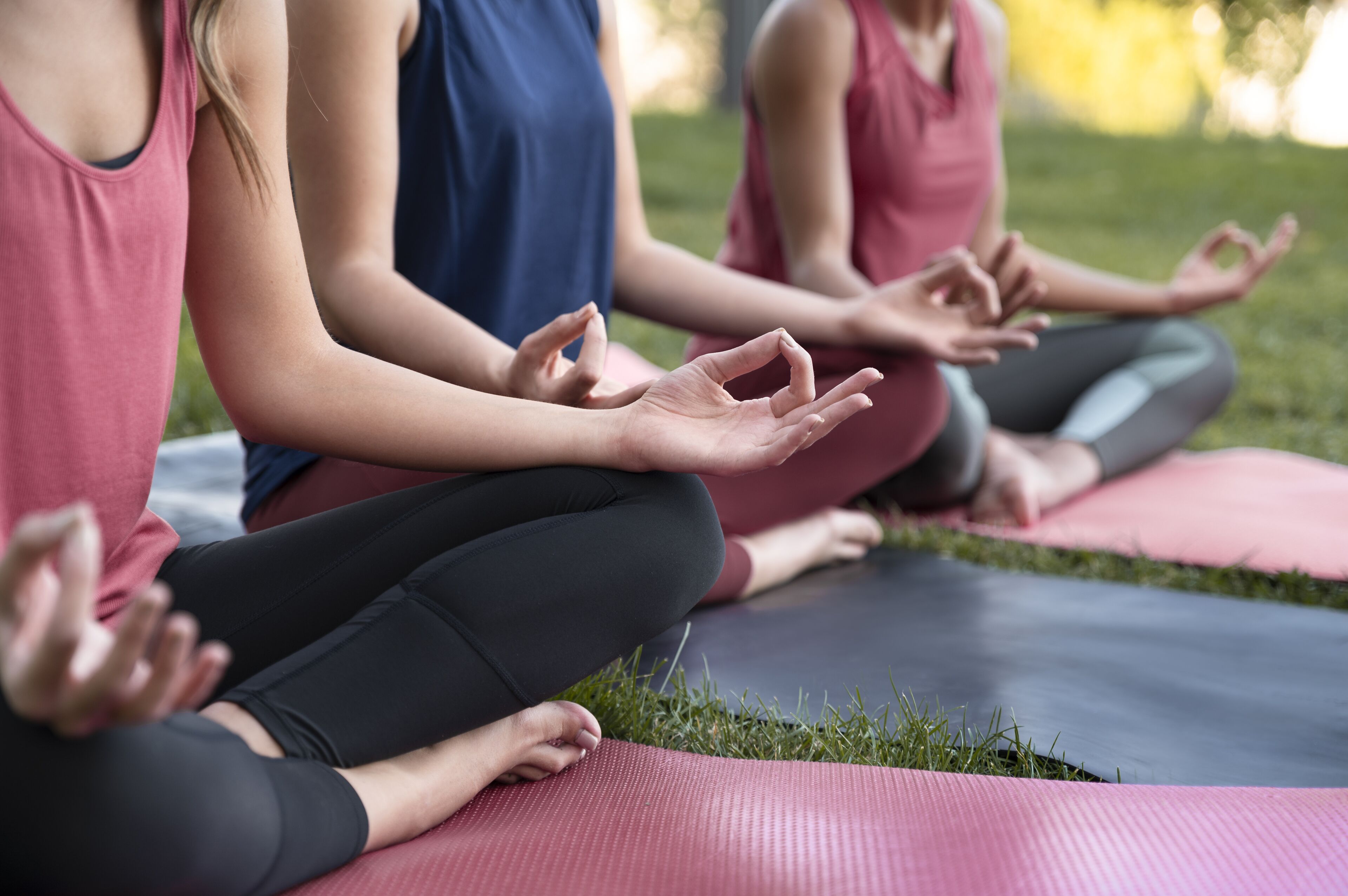 Three people sitting on yoga mats in a grassy outdoor area.