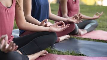 Three people sitting on yoga mats in a grassy outdoor area.