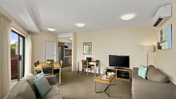 A modern living room with a sofa, coffee table, TV, and a dining area with a table and chairs.