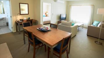 Une chambre d’hôtel avec une table à manger en bois, deux chaises, un canapé, une télévision et une lampe.