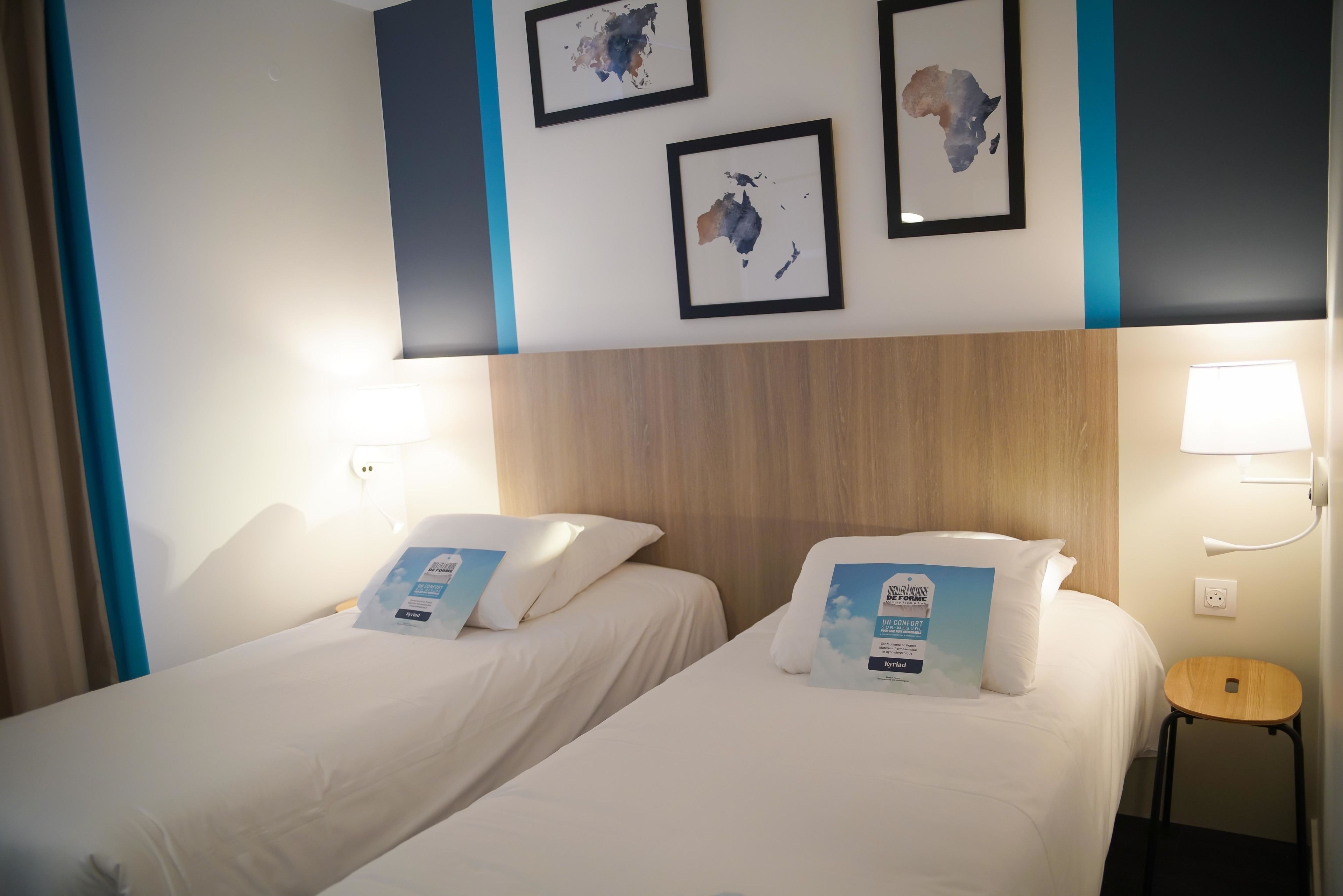 Une chambre d’hôtel avec deux lits, une tête de lit en bois et des cartes encadrées accrochées au mur.