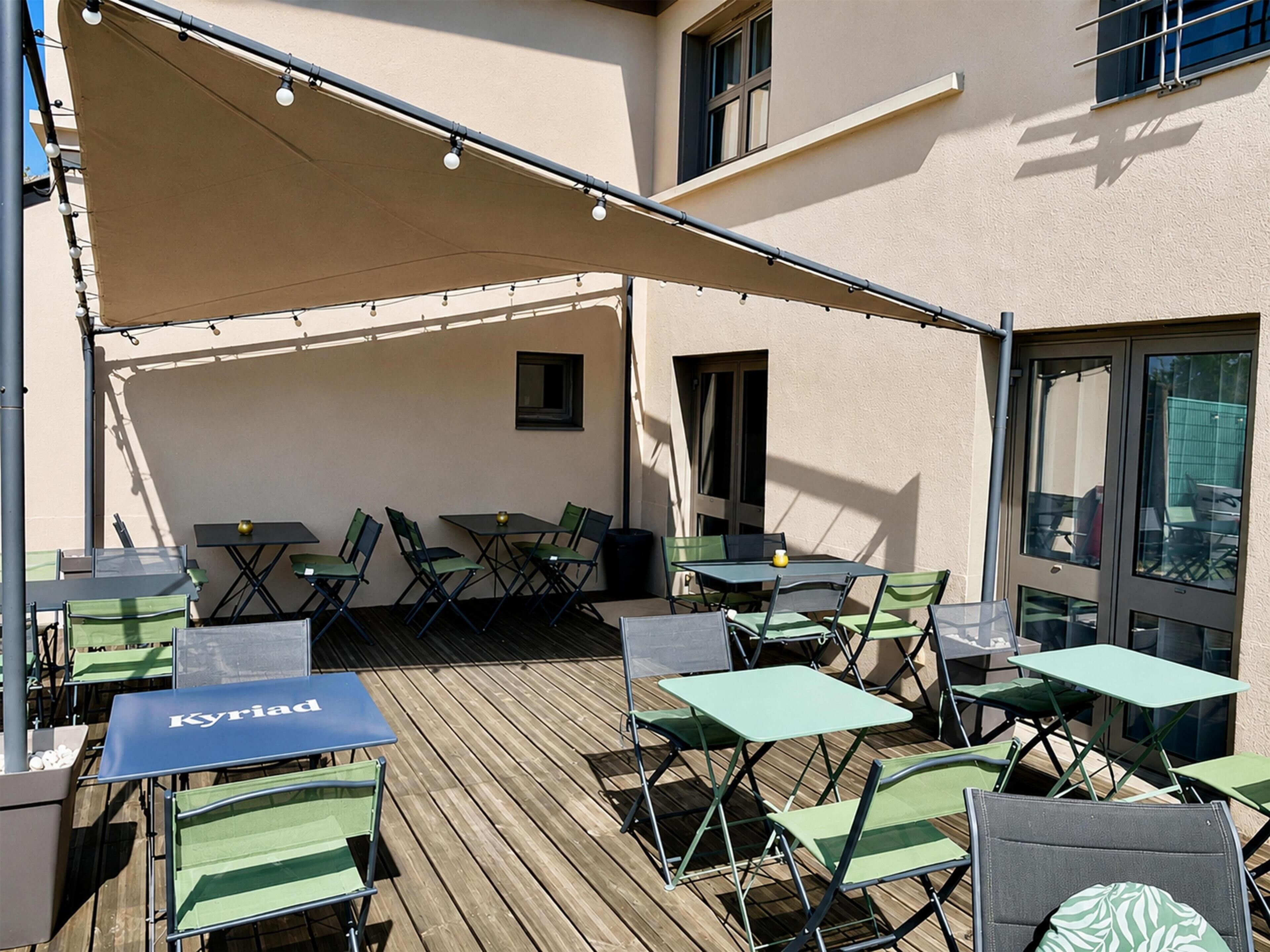 An outdoor patio with tables and chairs, a canopy providing shade, and a view of the building's exterior.