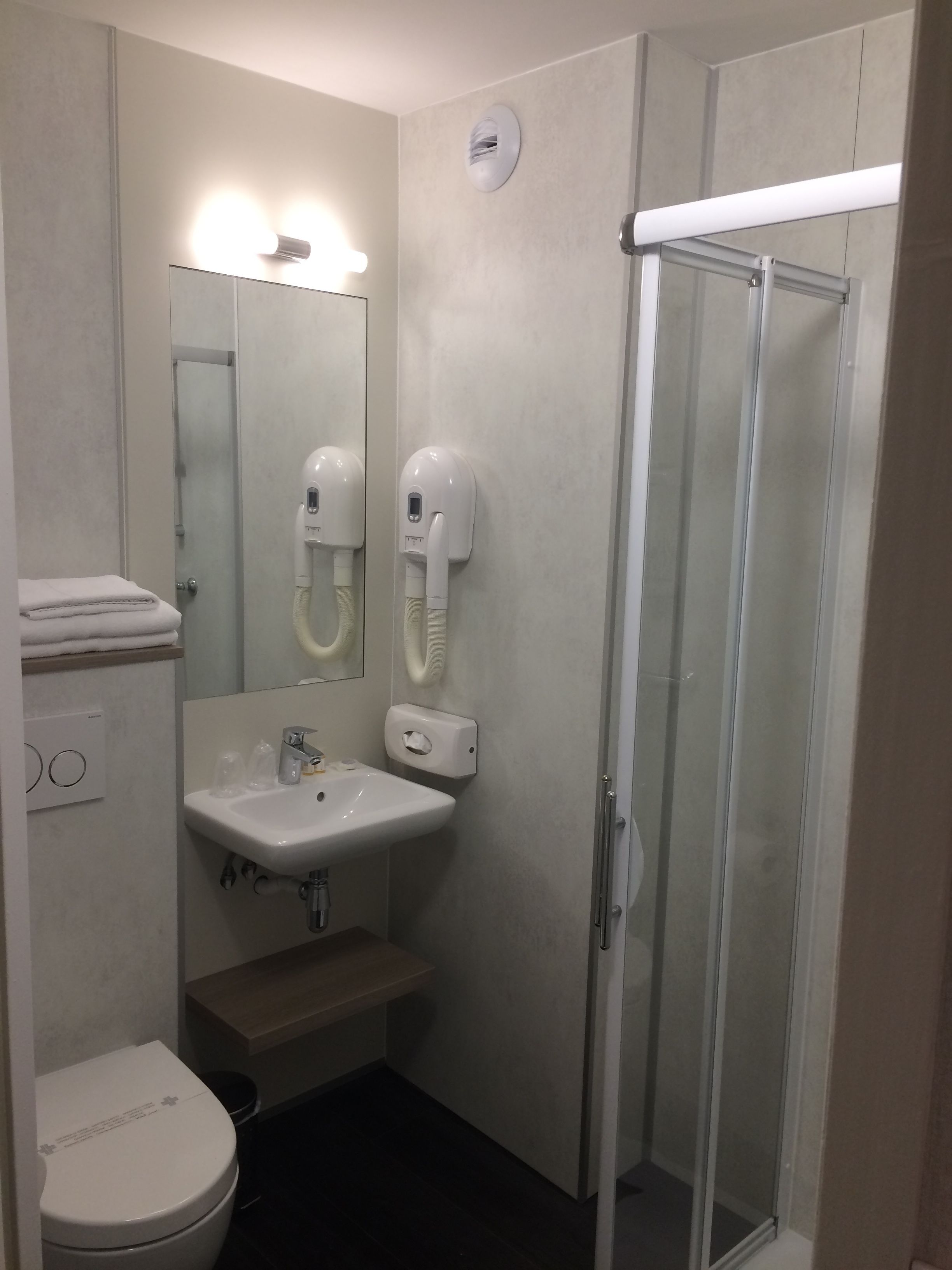 A modern bathroom with a glass shower enclosure, a sink with a mirror, and two hand dryers.