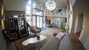 A spacious lobby with a large sofa, a coffee table, and a vending machine. There are chairs and a map on the wall.