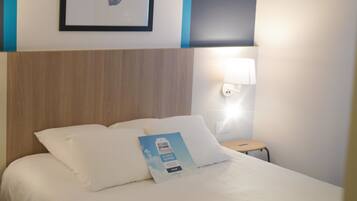 A hotel room with a bed, a framed map on the wall, a nightstand with a lamp, and a magazine on the bed.