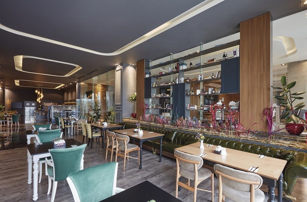Un restaurante moderno con mesas y sillas de madera, una zona de bar y diversos elementos decorativos y plantas.