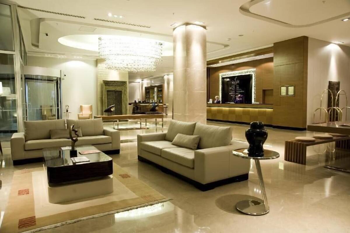 A modern lobby with a reception desk, two sofas, a coffee table, and a chandelier.