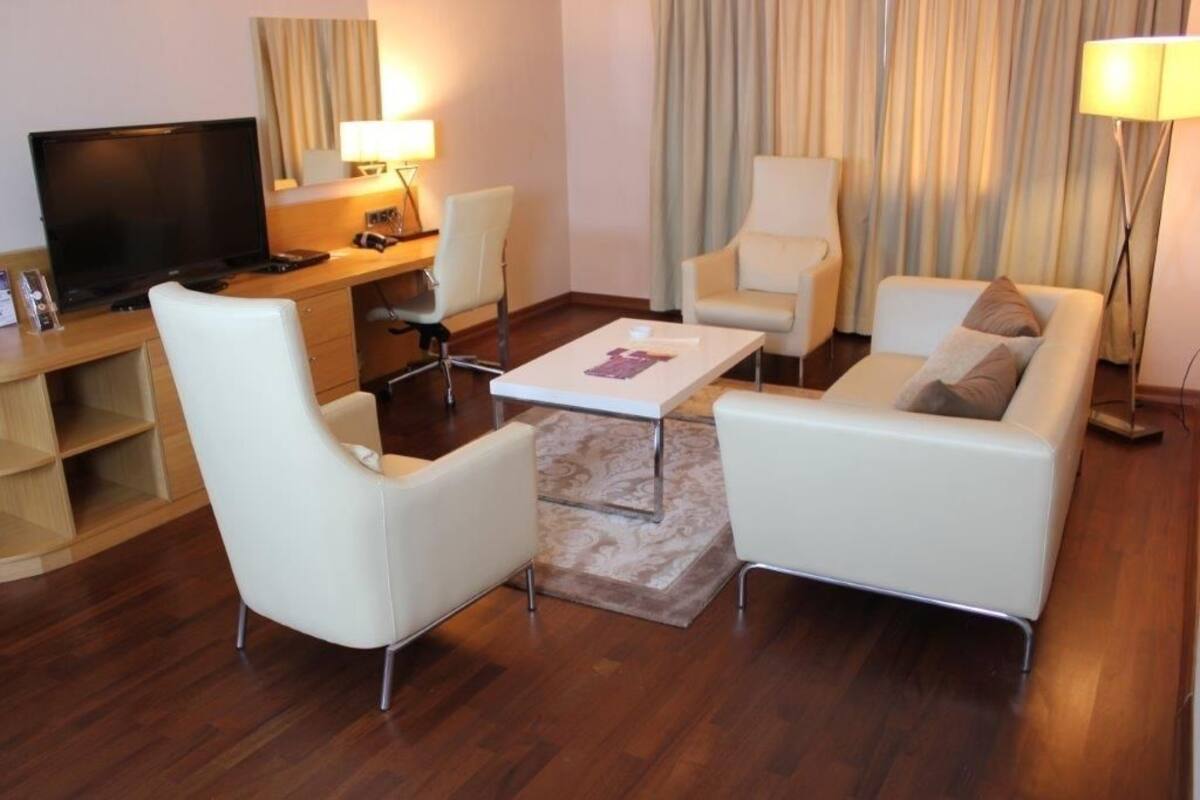 A modern living room with a flat-screen TV, a desk, and two white armchairs.