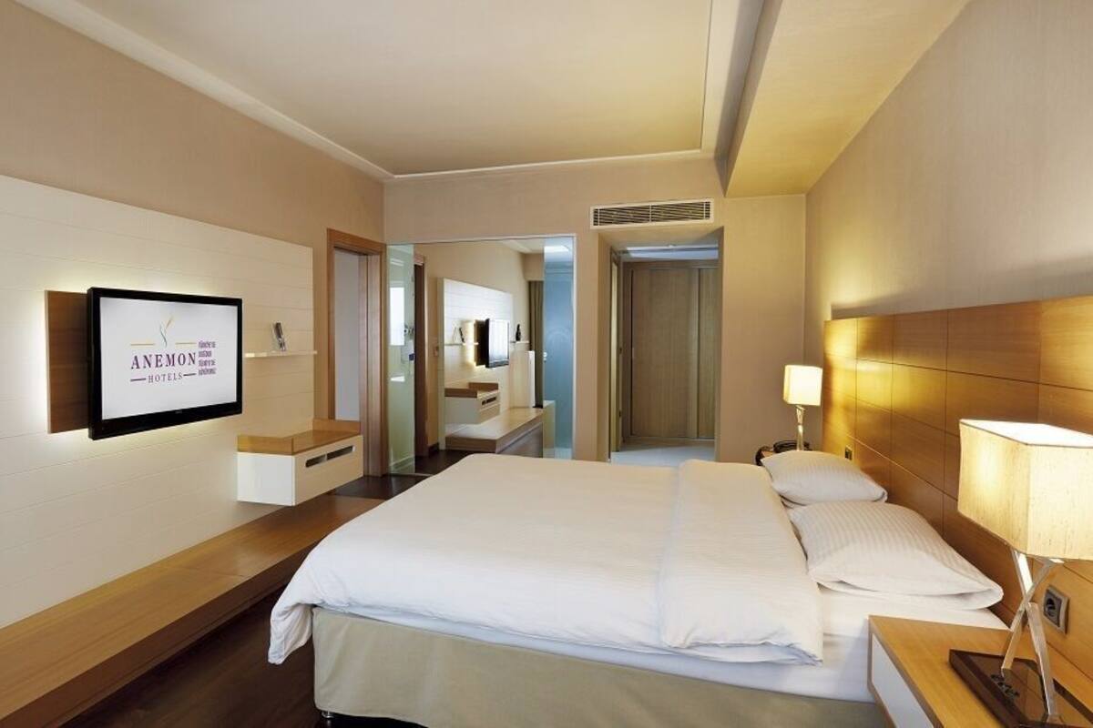 A hotel room with a bed, bedside table, lamp, and a television mounted on the wall.