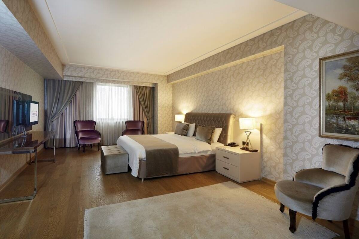A modern hotel room with a large bed, a desk, a chair, and a TV.