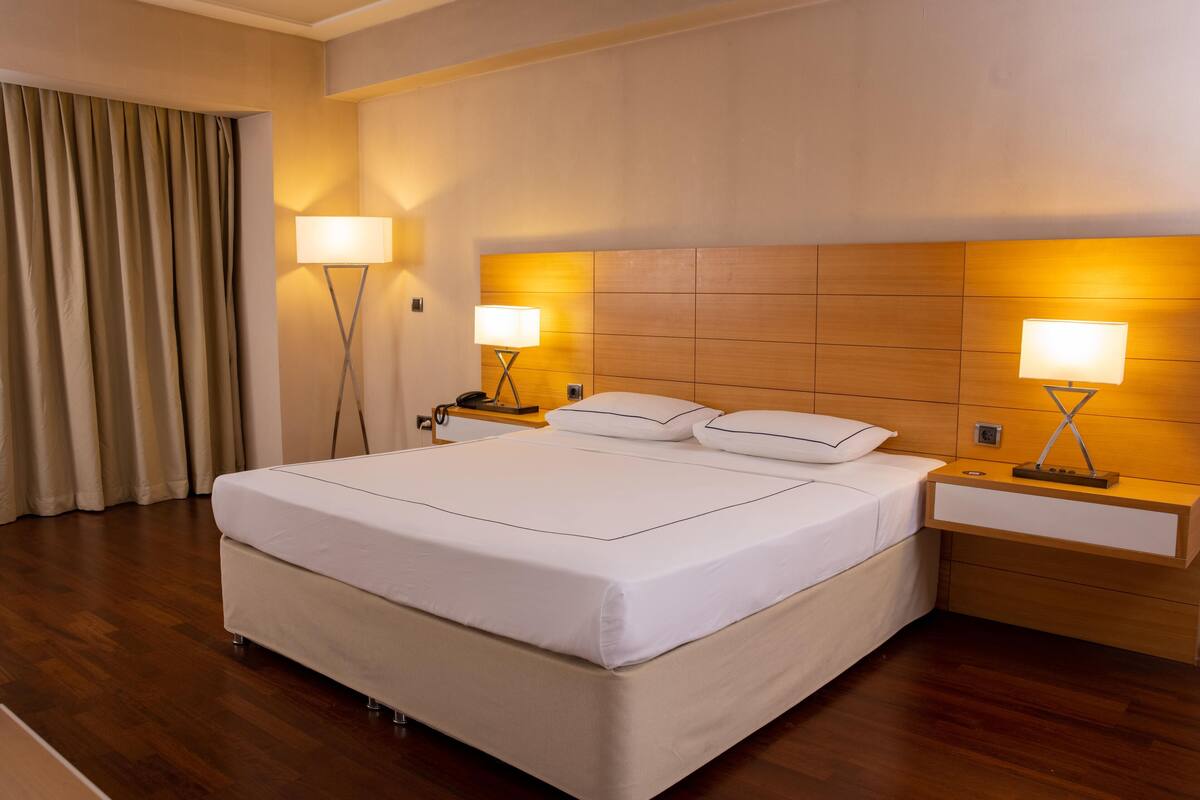 A hotel room with a large bed, two bedside tables with lamps, and a wooden headboard.