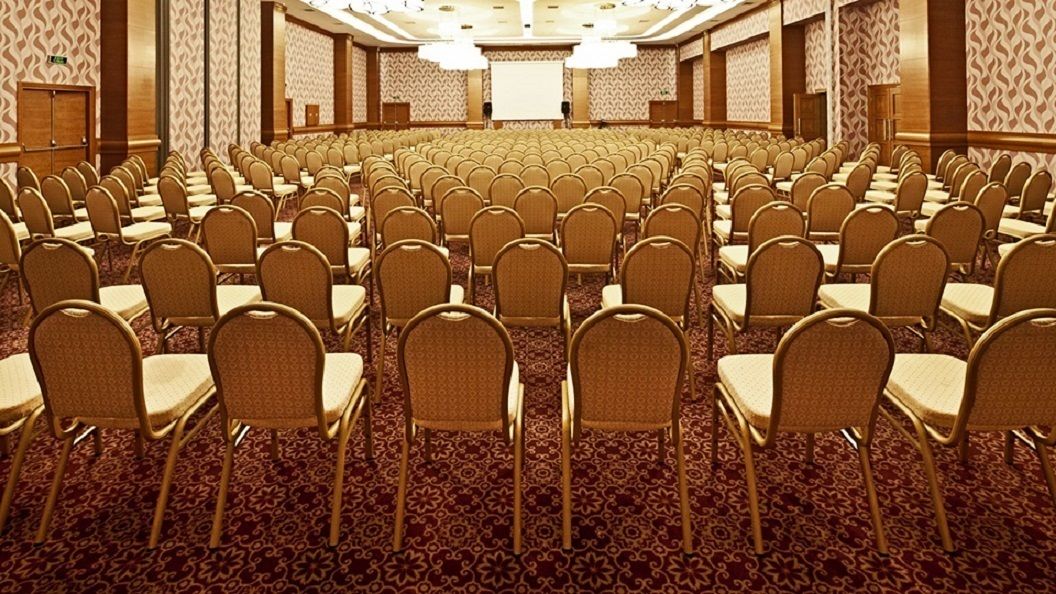 Een vergaderzaal met rijen stoelen en een groot scherm aan de voorkant.